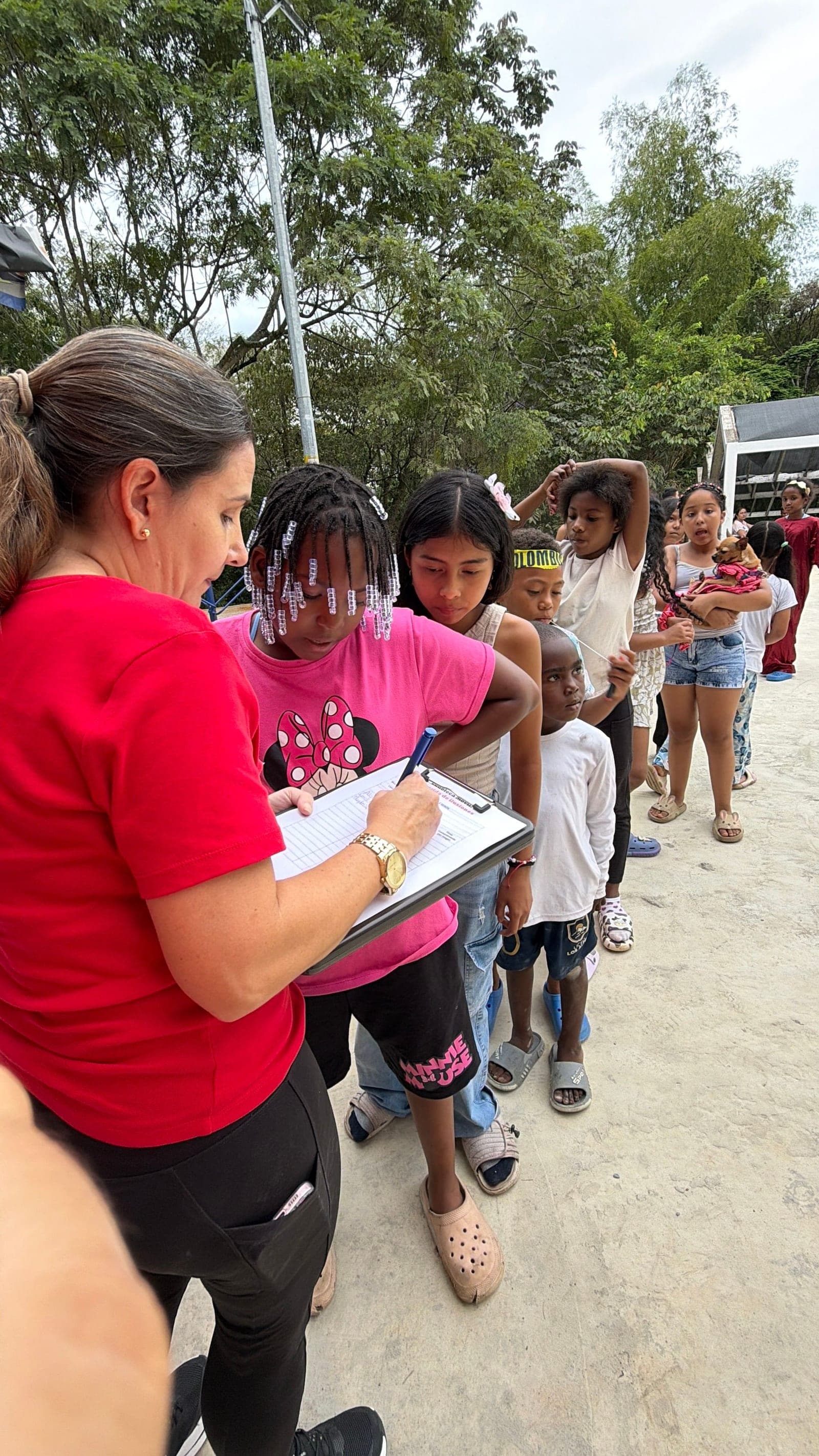 Una gestora anota el control de asistencia en una tabla mientras los niños esperan en fila