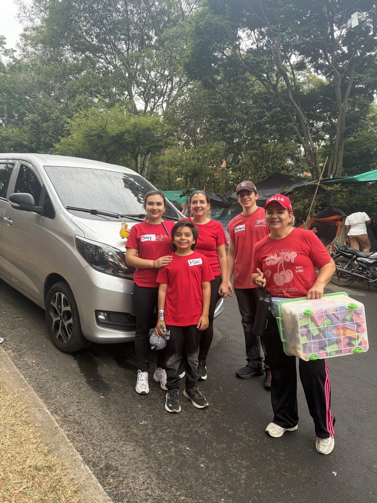 El equipo de gestores voluntarios con camisetas rojas junto al vehículo, cargando una caja de material didáctico